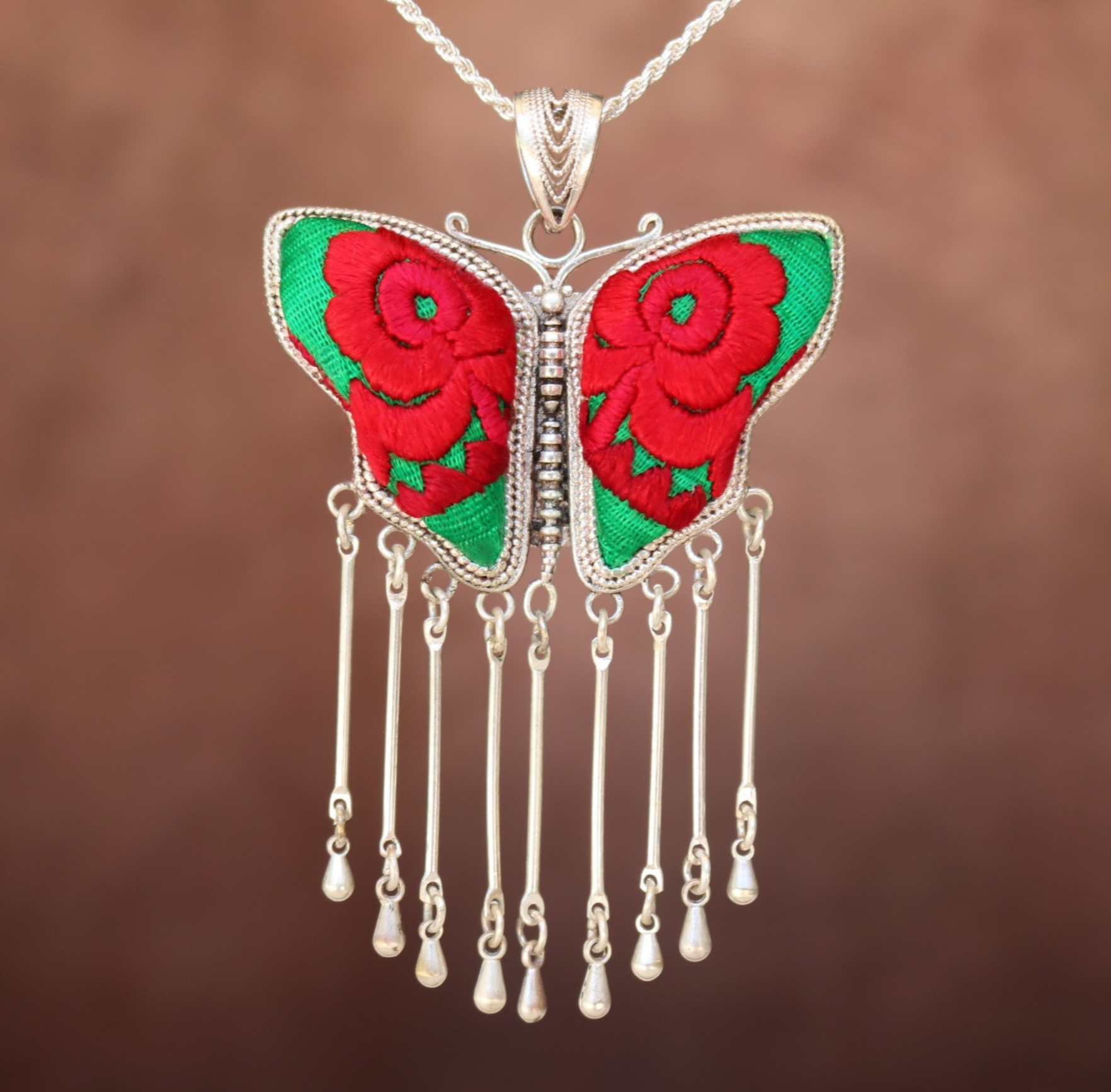 A silver-plated bronze pendant necklace with red and green hand-embroidered butterfly and floral designs, featuring a vintage look.