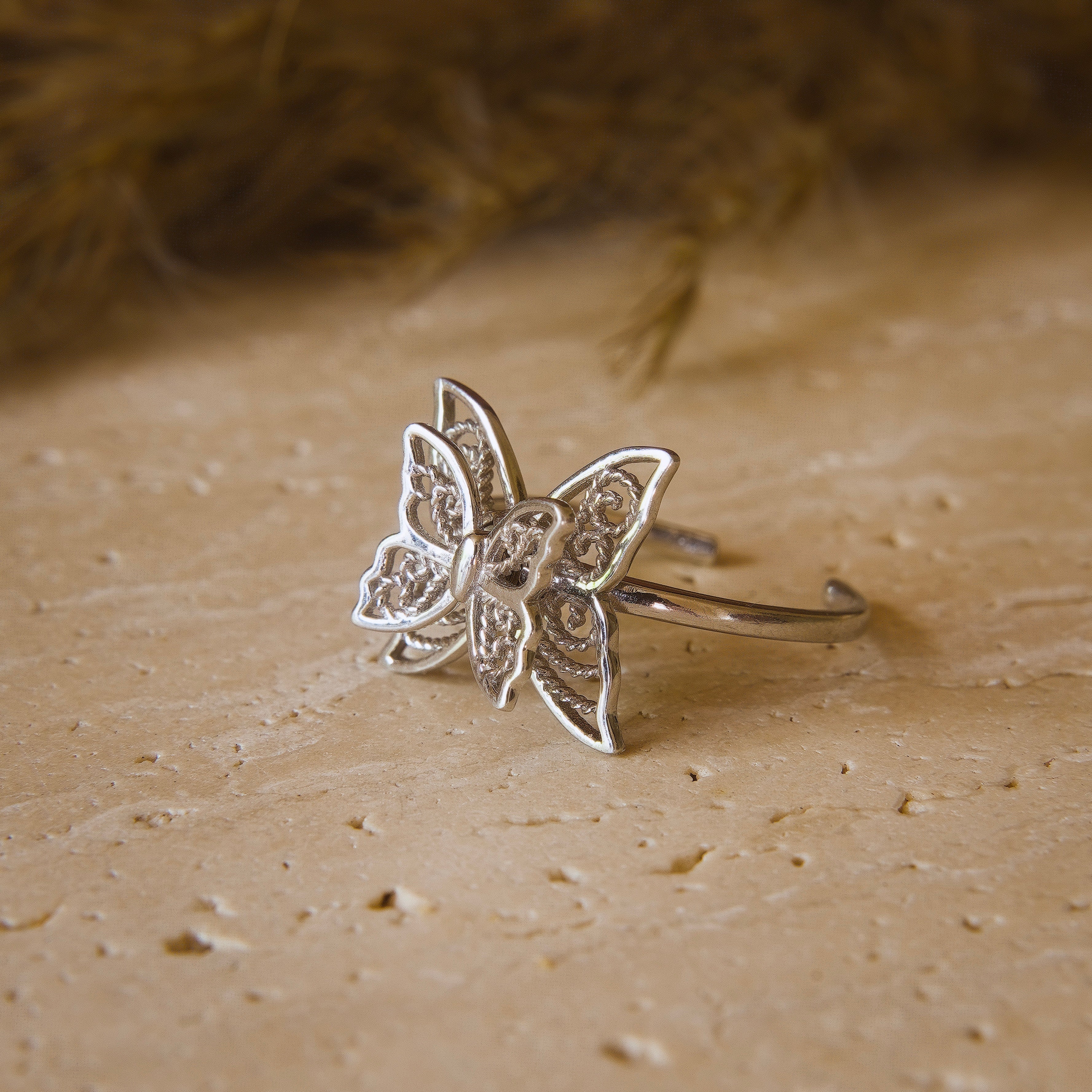 Silver butterfly ring on a textured beige surface