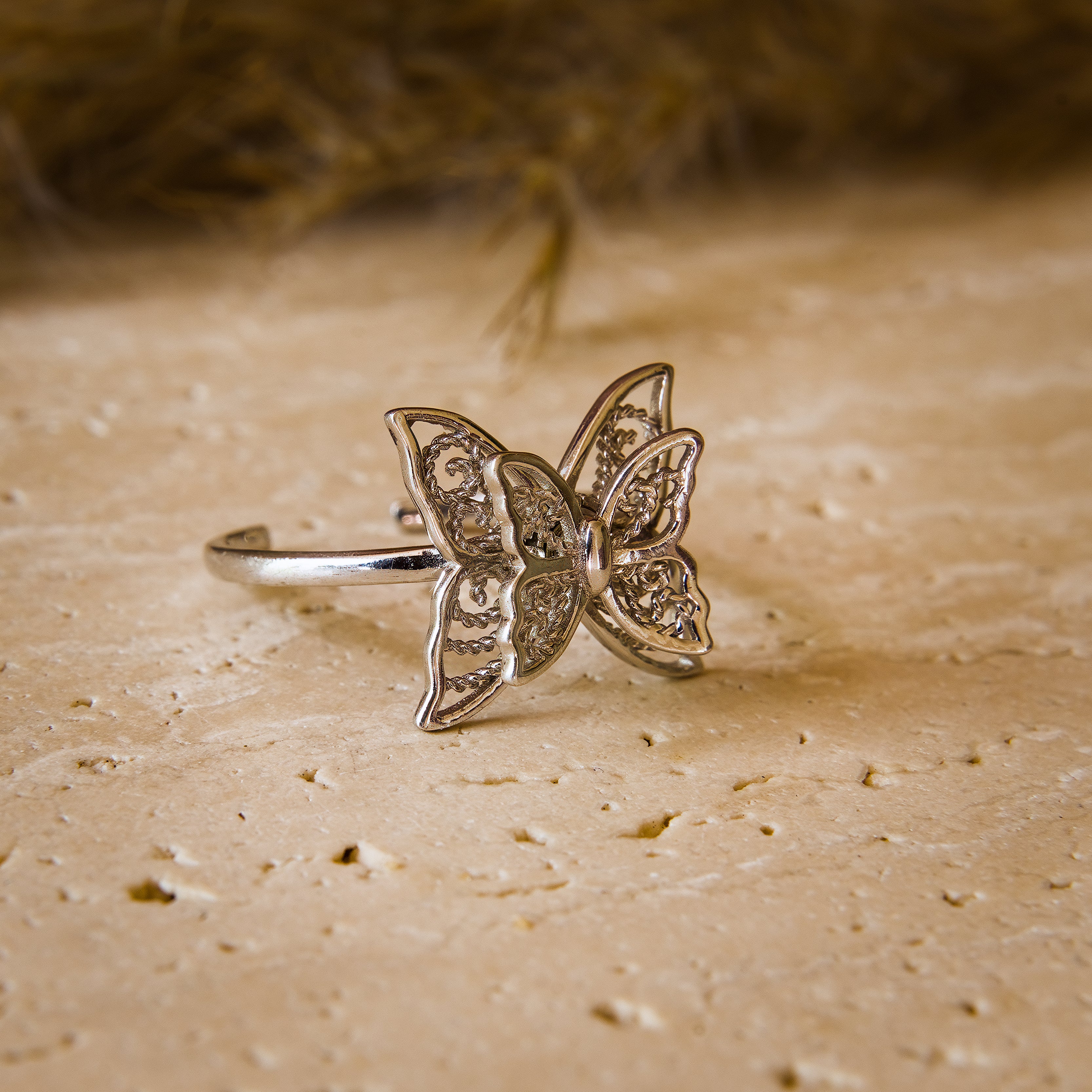 Silver butterfly ring on a textured beige surface
