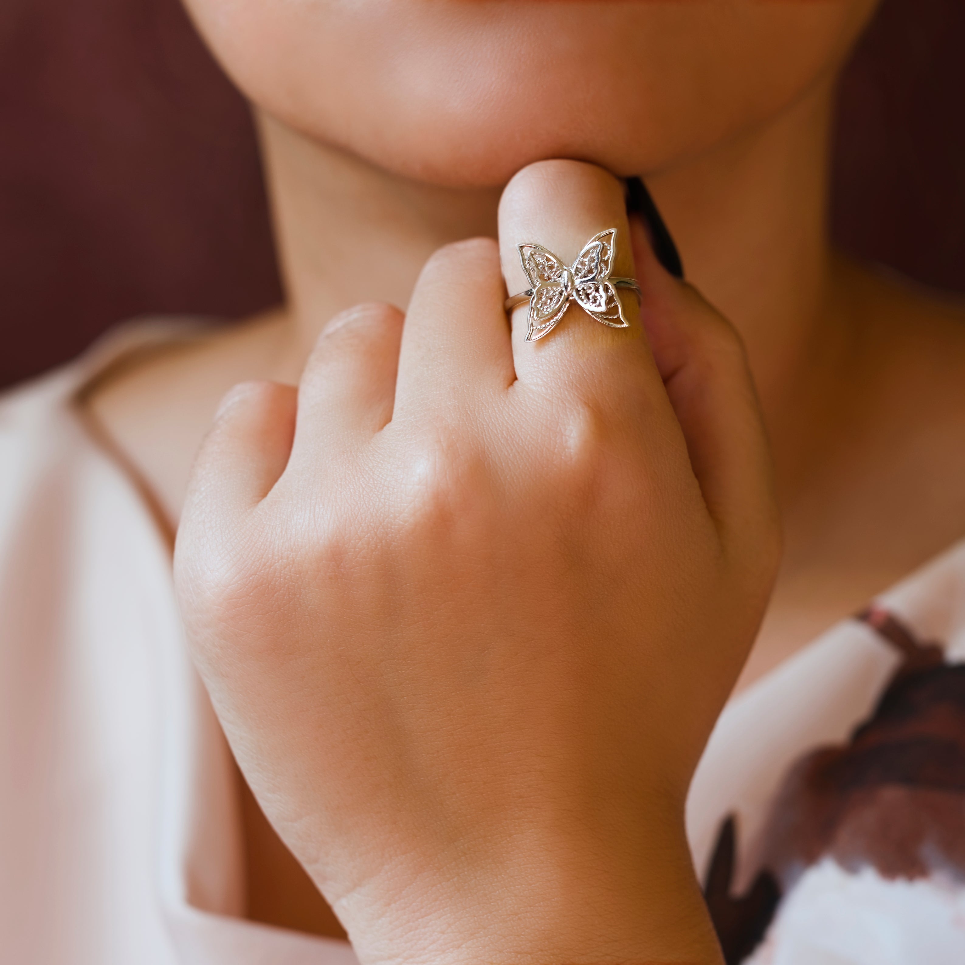 Close-up of a hand wearing a butterfly-shaped ring with a blurred background
