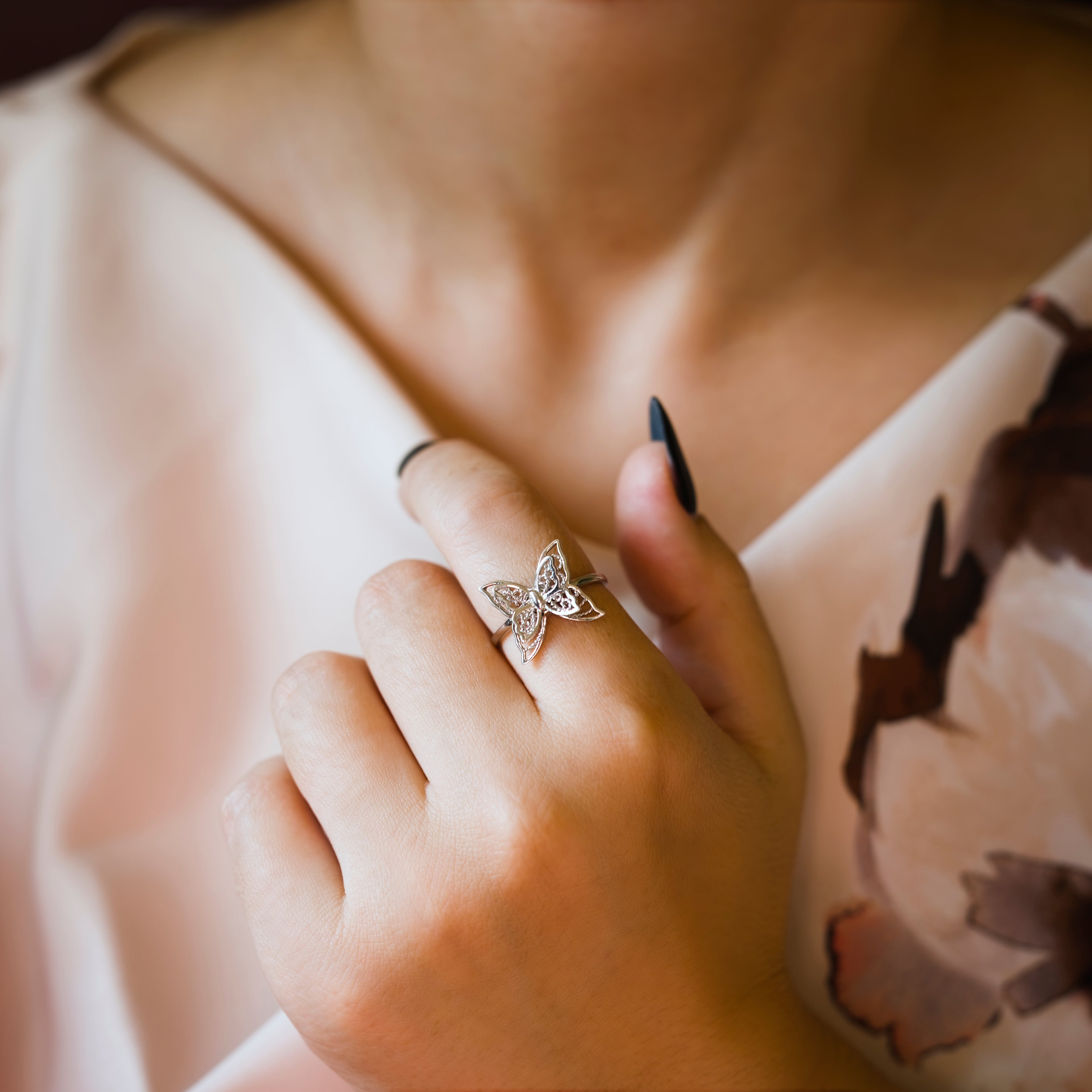 Close-up of a hand wearing a butterfly-shaped ring with a blurred background
