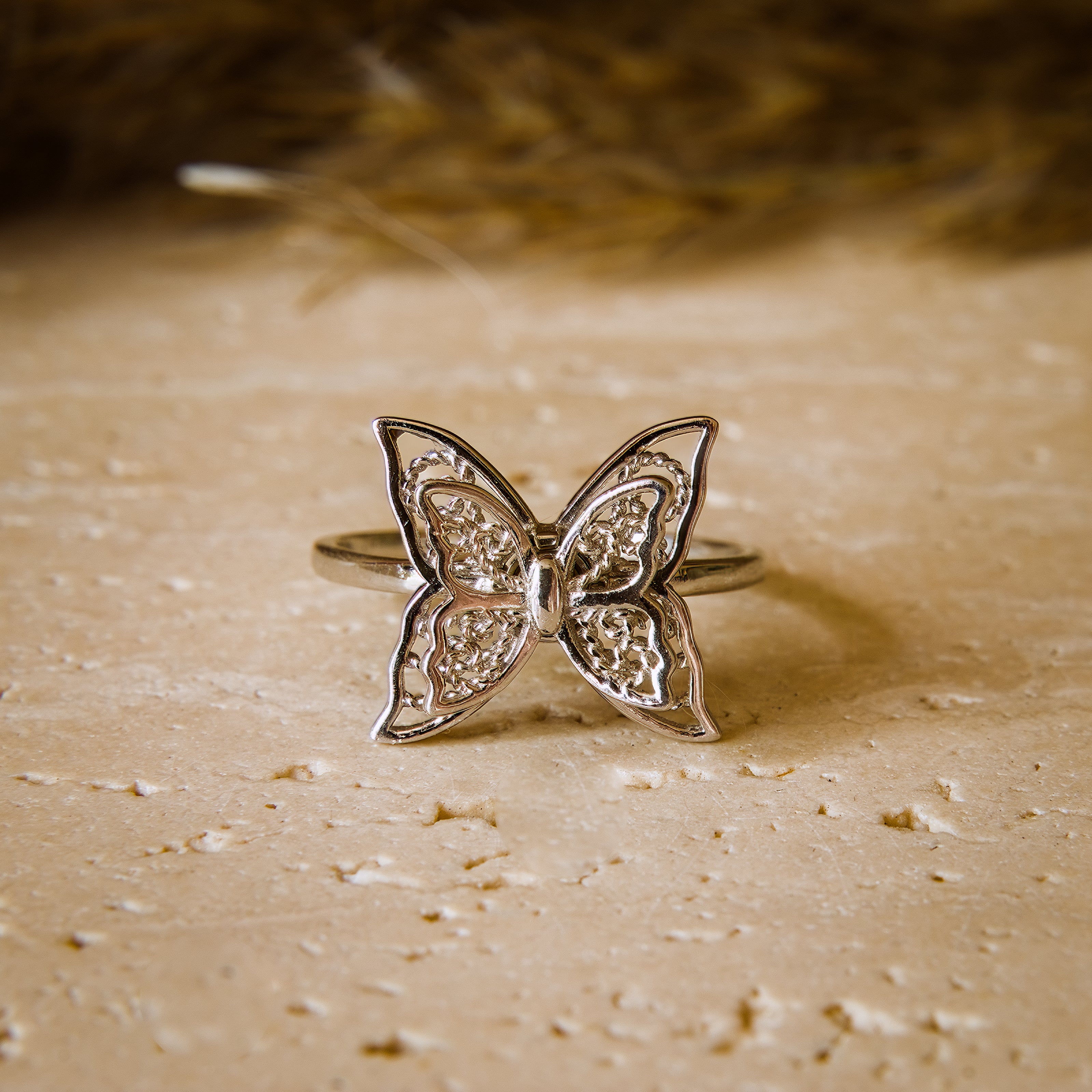 Silver butterfly ring on a textured beige surface